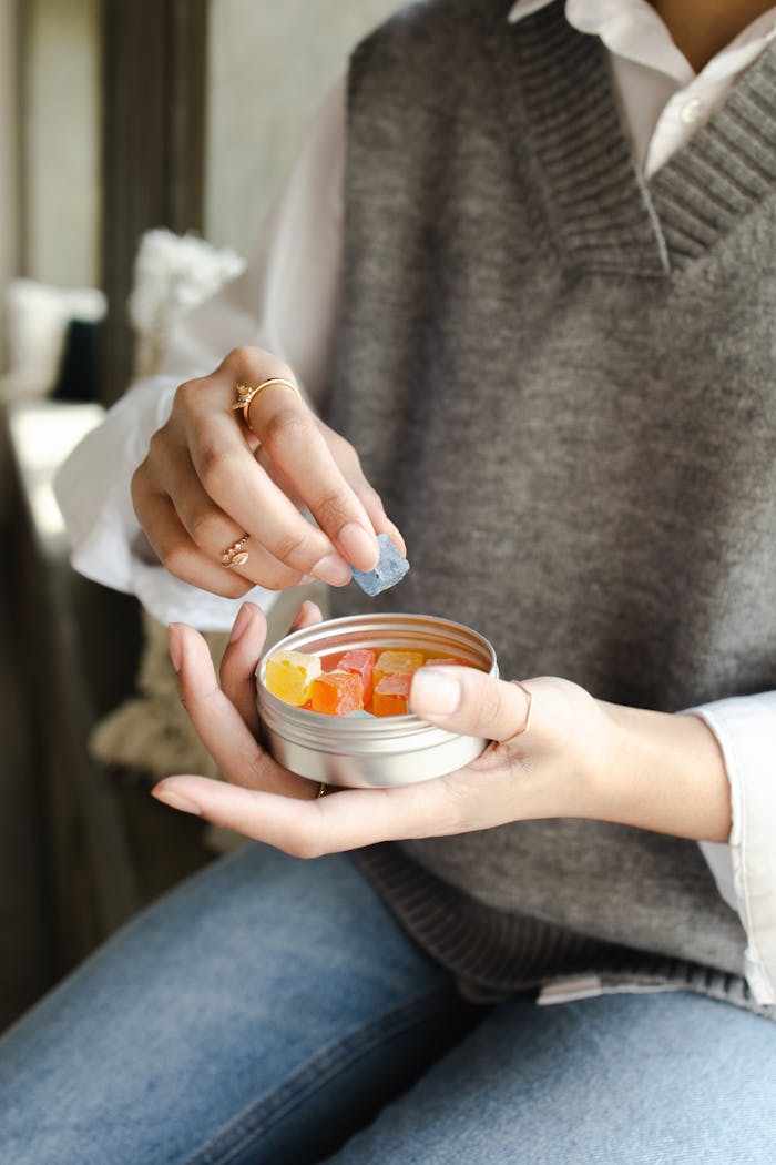Close-up of a hand holding a tin of colorful CBD gummies indoors.