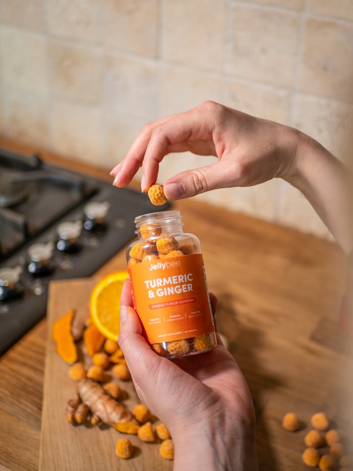 Close-up of hands holding turmeric and ginger gummies with an orange background.